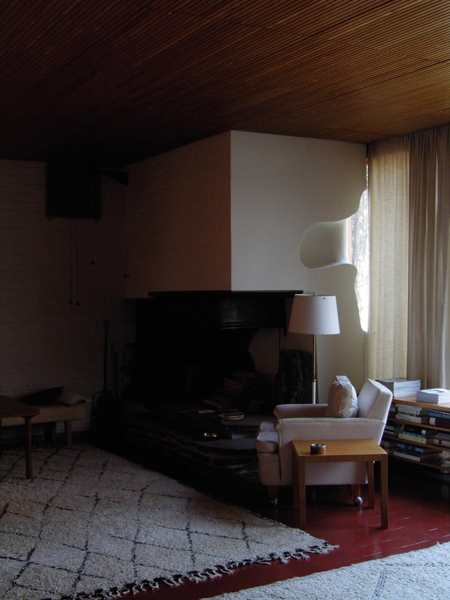 Il soggiorno di Villa Mairea con il camino bianco, il soffitto a doghe di legno, tappeti e poltrona
