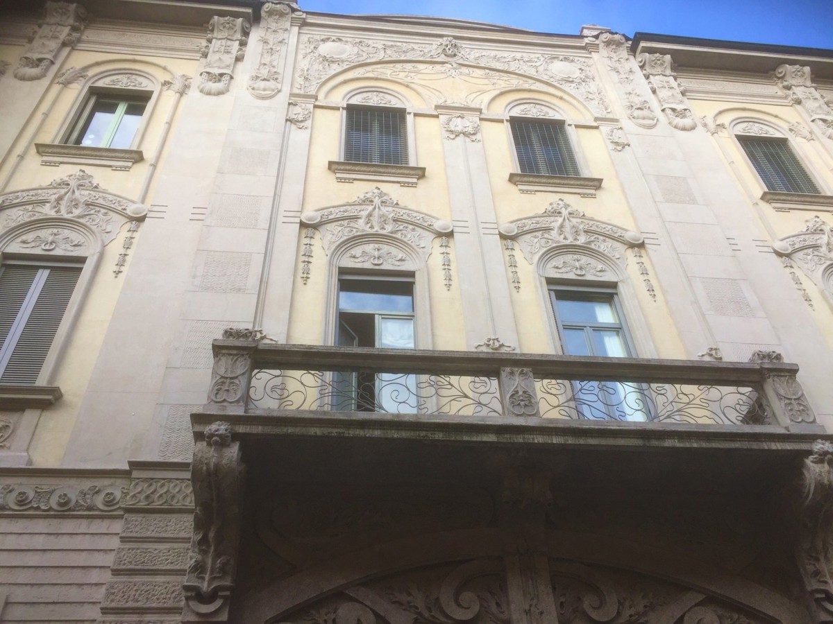 Dettaglio della facciata di casa Beretta a Pavia con le decorazioni in cemento sopra le finestre e il balcone in ferro battuto