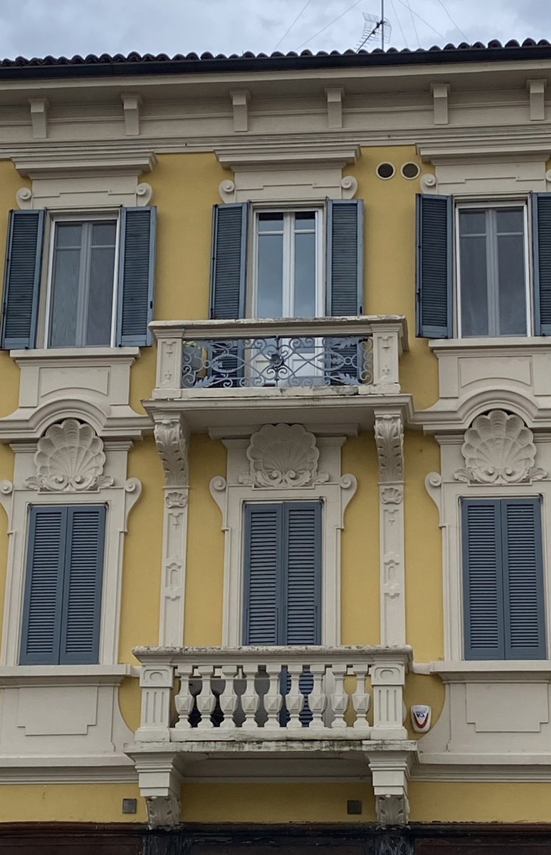 Dettaglio della facciata gialla di casa Gandini a Pavia, con i balconi e le cornici delle finestre