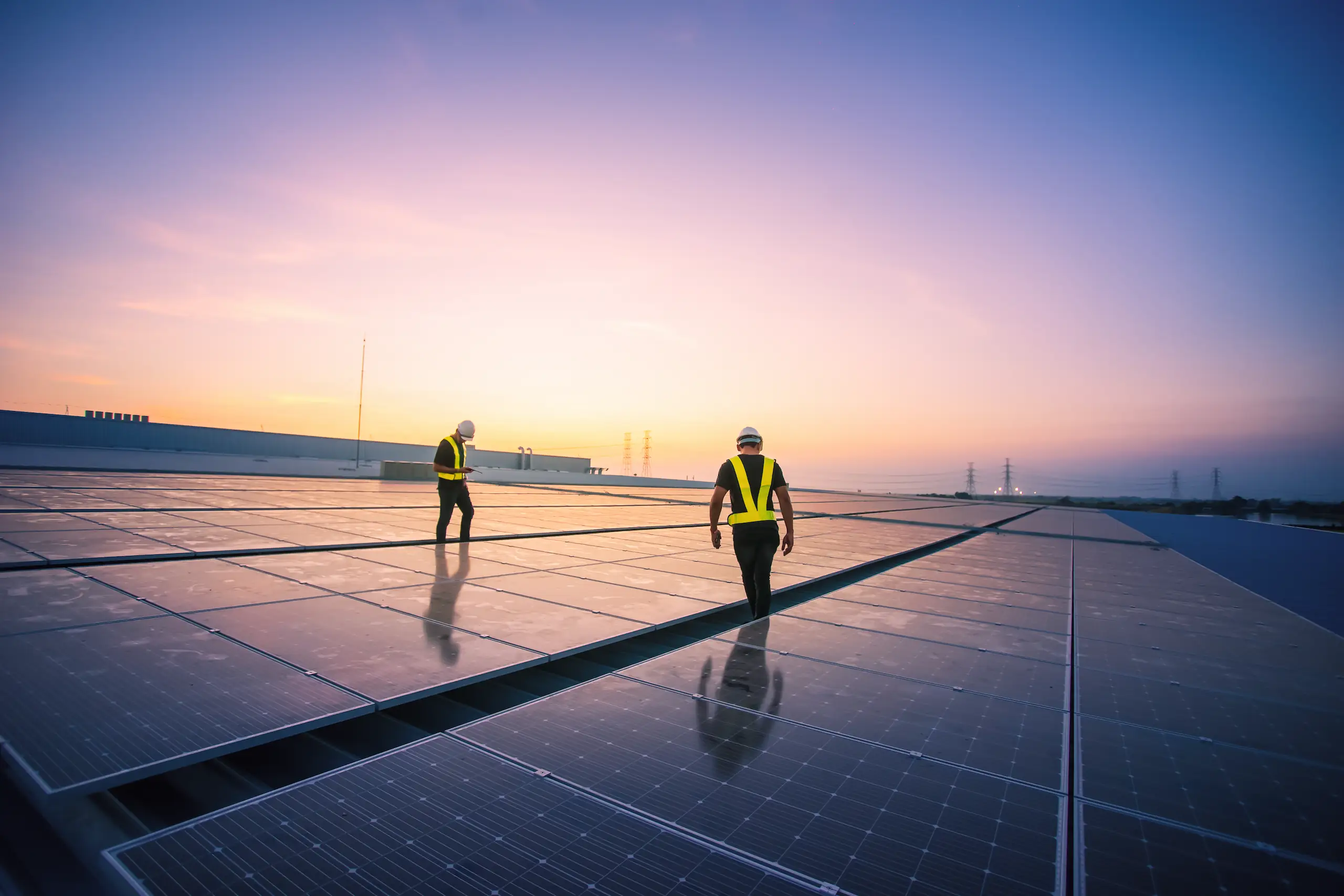Zwei Ingenieuren prüfen die Installation von Solarzellen auf dem Dach einer Fabrik am Morgen.