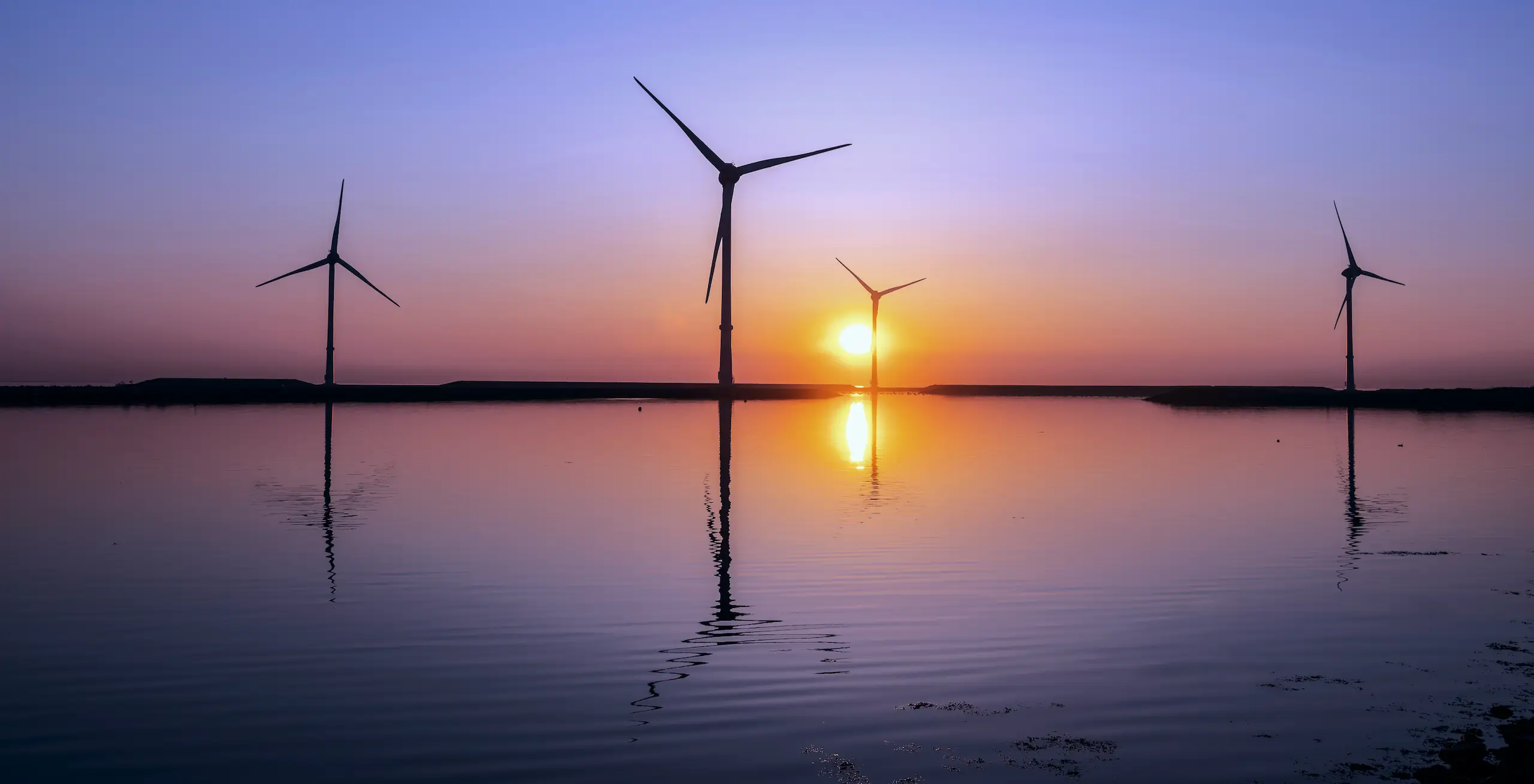 Windturbinen und bunter Sonnenaufgang, der sich im Wasser spiegelt.
