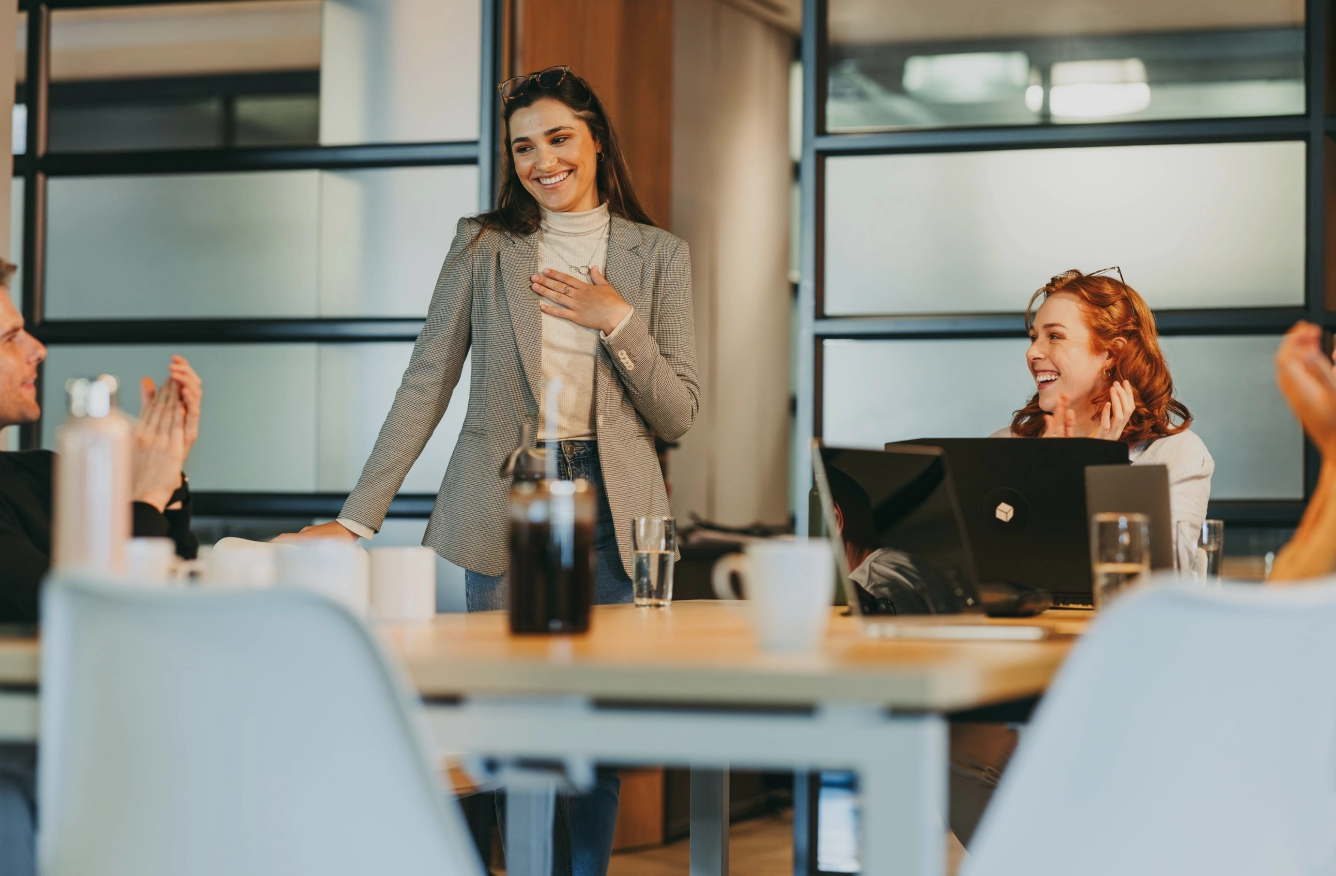Direkteinstieg Frau im Business-Outfit präsentiert lächelnd in einem Meetingraum, Kollegin mit Laptop daneben.