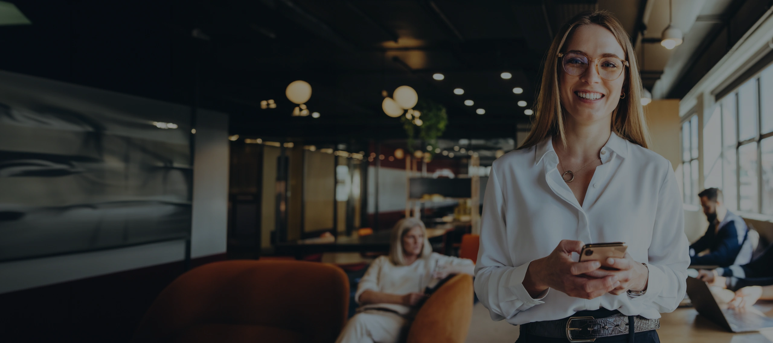 Studierende Eine lächelnde Studierende in einem modernen Co-Working-Space, die ein Smartphone hält.
