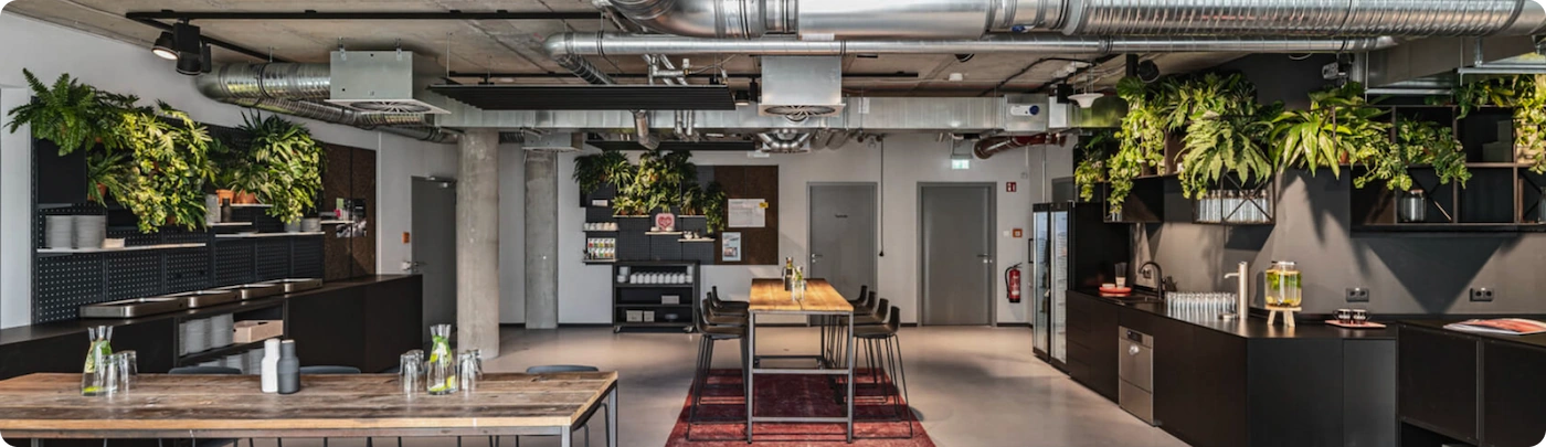 Professionelles Foto einer Büroküche im Industriestil mit offenem Raumkonzept und grünen Pflanzen an den Wänden.