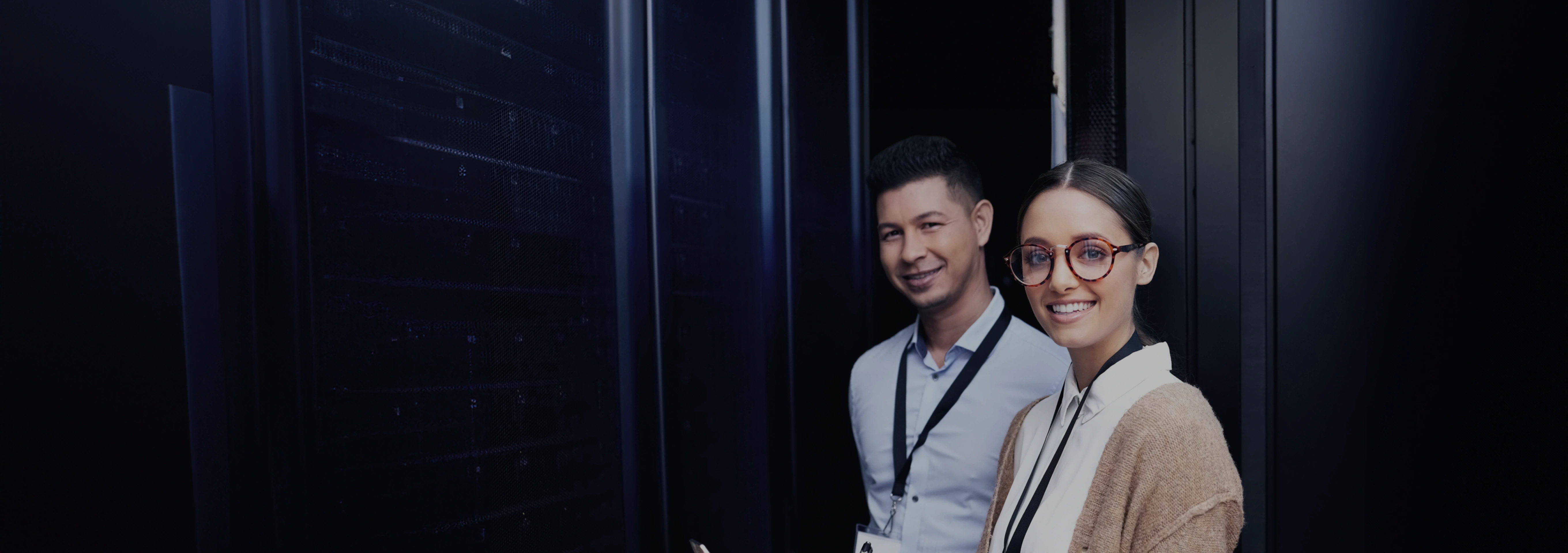 Zwei Personen in einem Serverraum, lächelnd und in professioneller Kleidung, mit Serverracks im Hintergrund.
