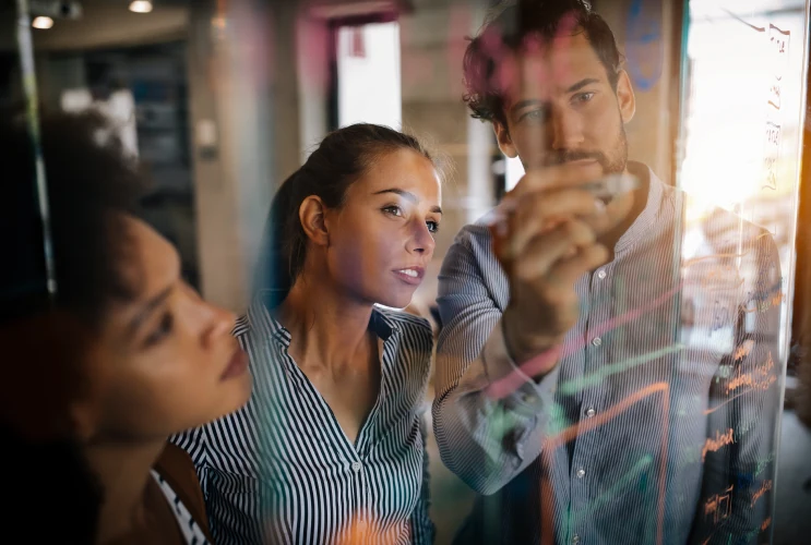 Ideenfindung im Team Ein Mann und zwei Frauen brainstormen auf einem Glasboard im Büro.