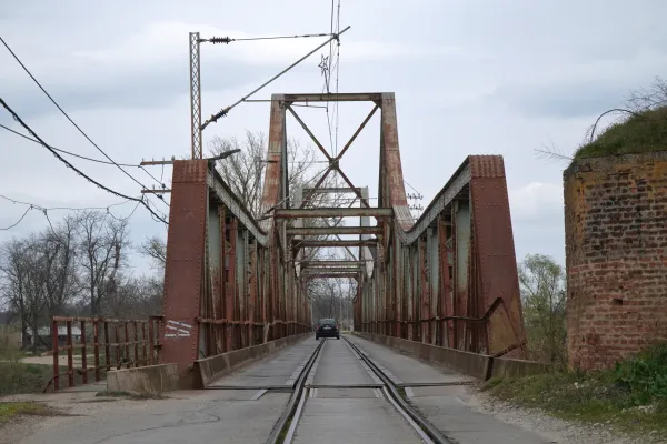 Любичевский мост, железный мост через реку Мораву недалеко от Пожареваца, Сербия, с проезжающим по нему автомобилем, видны ржавые металлические балки и рельсы.