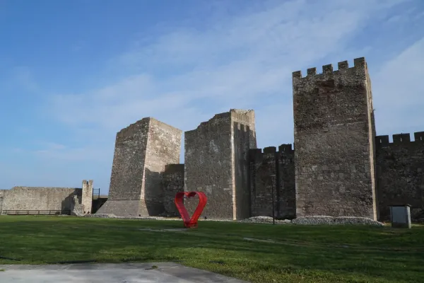 Die Smederevo Festung in Serbien mit ihren hohen Steinmauern und Türmen, daneben eine leuchtend rote Herzskulptur auf einem grünen Rasen.