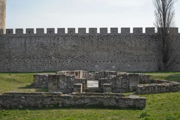 Antiguos cimientos y muros de piedra sobre el césped con el alto muro de piedra de la Fortaleza de Smederevo al fondo, Serbia.
