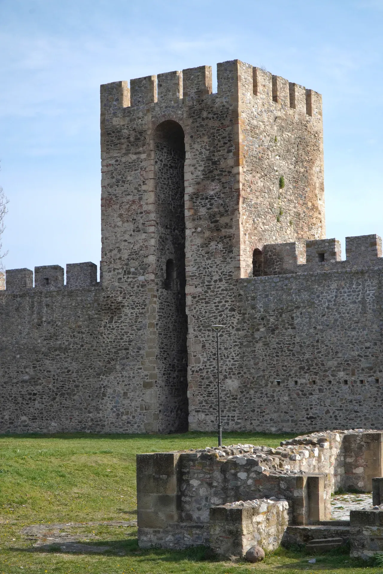 Die Smederevo Festung mit ihren imposanten Steinmauern und einem Turm unter blauem Himmel, mit grasbewachsenem Vordergrund und Ruinen.