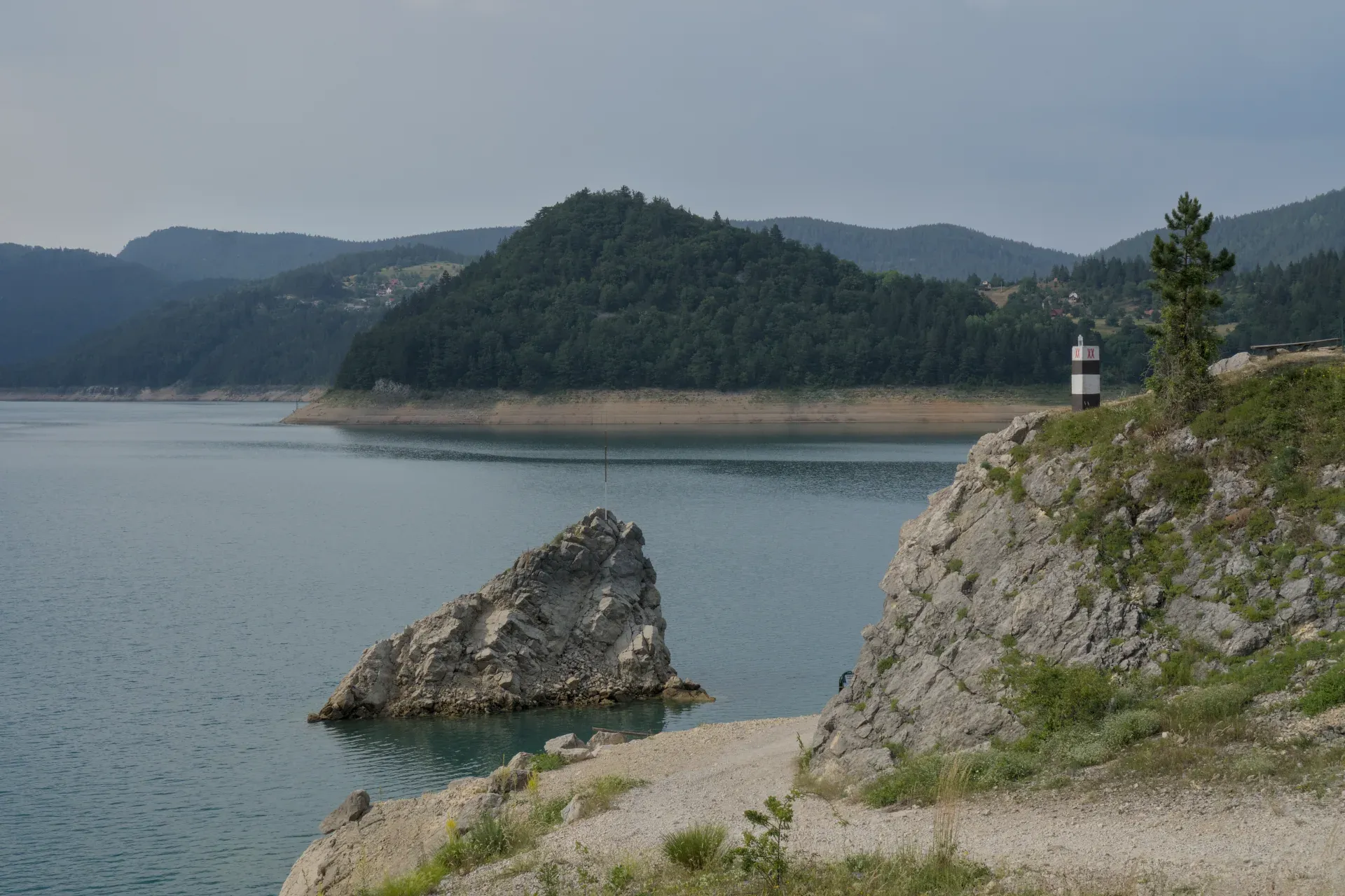 Lac Zaovine dans le parc national de Tara, Serbie, avec des montagnes vertes, des rochers et un phare.