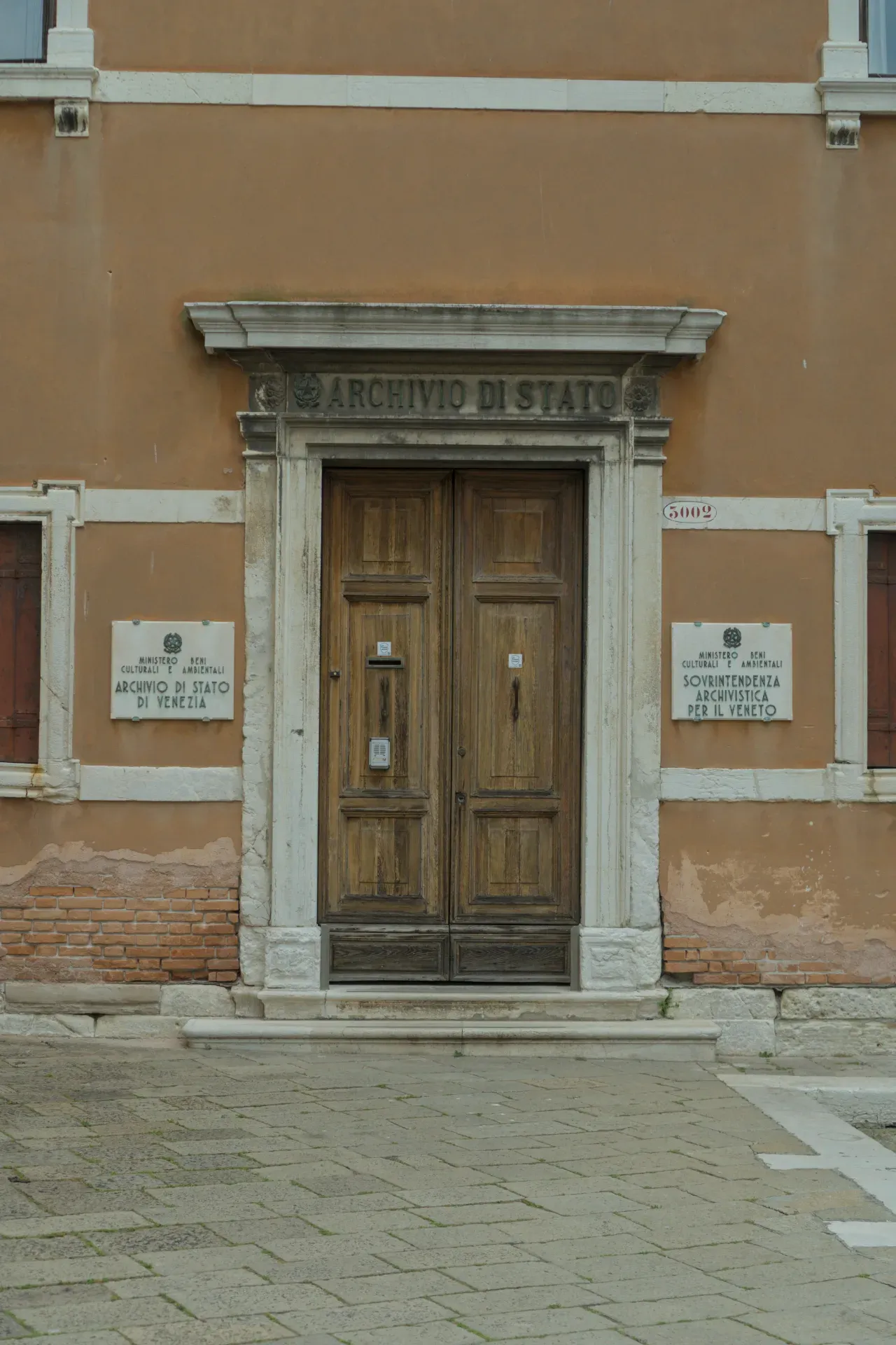 Eine breite, alte Holztür am Eingang des Archivio di Stato in Venedig, eingerahmt von Steinsäulen und einer ockerfarbenen Fassade.