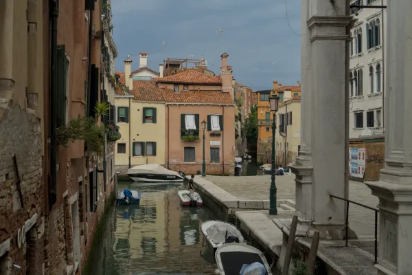 Ein Venedig-Kanal mit verschiedenen Booten, umgeben von farbenfrohen historischen Gebäuden und einem bewölkten Himmel.