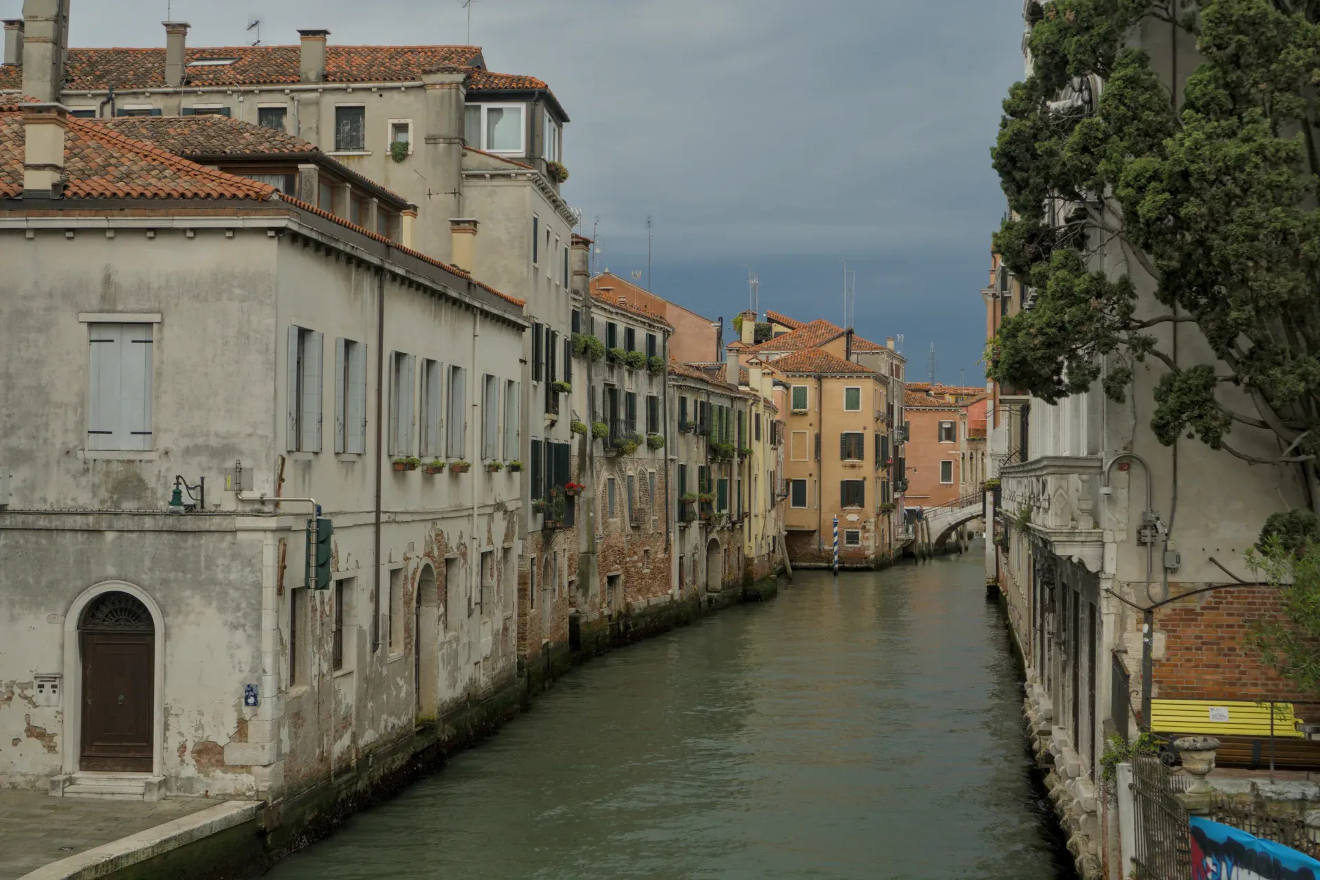 A narrow canal in Venice with historic buildings and a dramatic, cloud-filled sky.