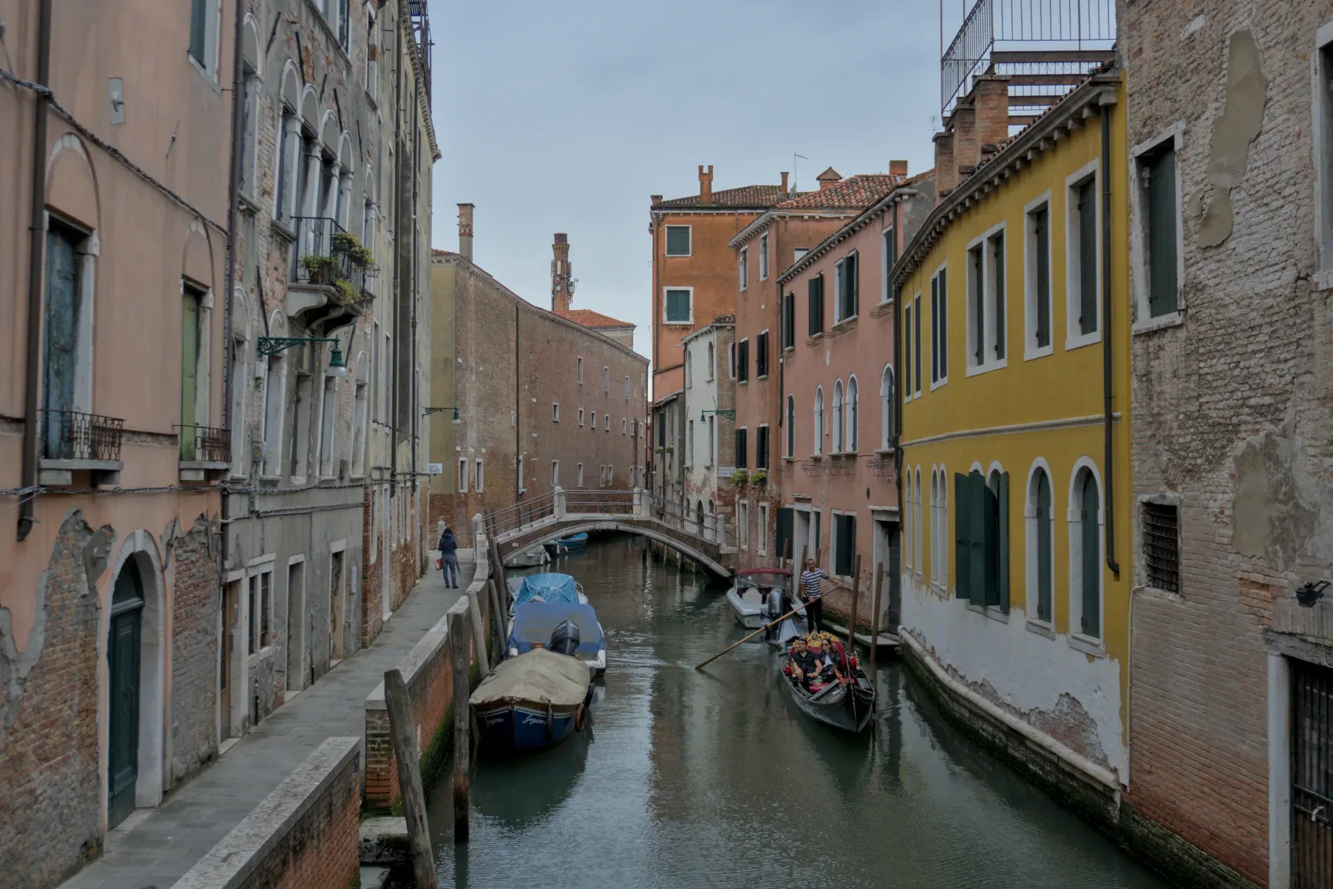 Ein schmaler Kanal in Venedig mit einer Gondel, gesäumt von bunten historischen Gebäuden und einem Gehweg.