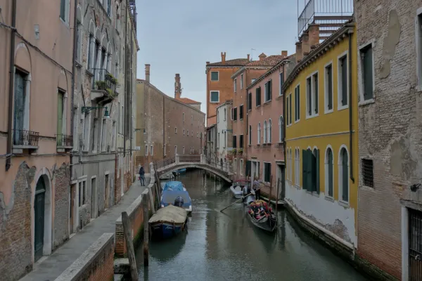 Ein schmaler Kanal in Venedig mit einer Gondel, gesäumt von bunten historischen Gebäuden und einem Gehweg.