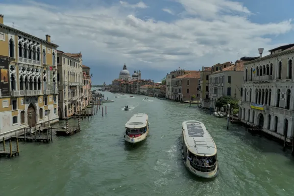 Due barche navigano lungo il Canal Grande a Venezia, fiancheggiate da palazzi storici e una cupola sullo sfondo.