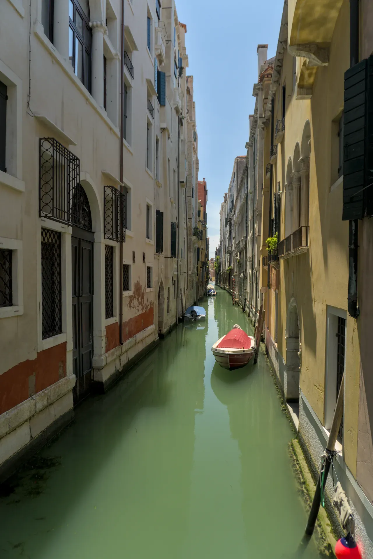 Stretto vicolo veneziano con una barca in acqua verde smeraldo, circondato da edifici storici.