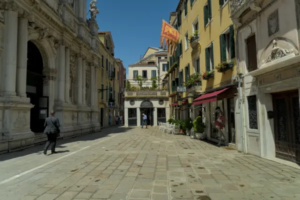 Un vicolo acciottolato a Venezia con edifici storici, un uomo in giacca e cravatta e uno stendardo rosso.