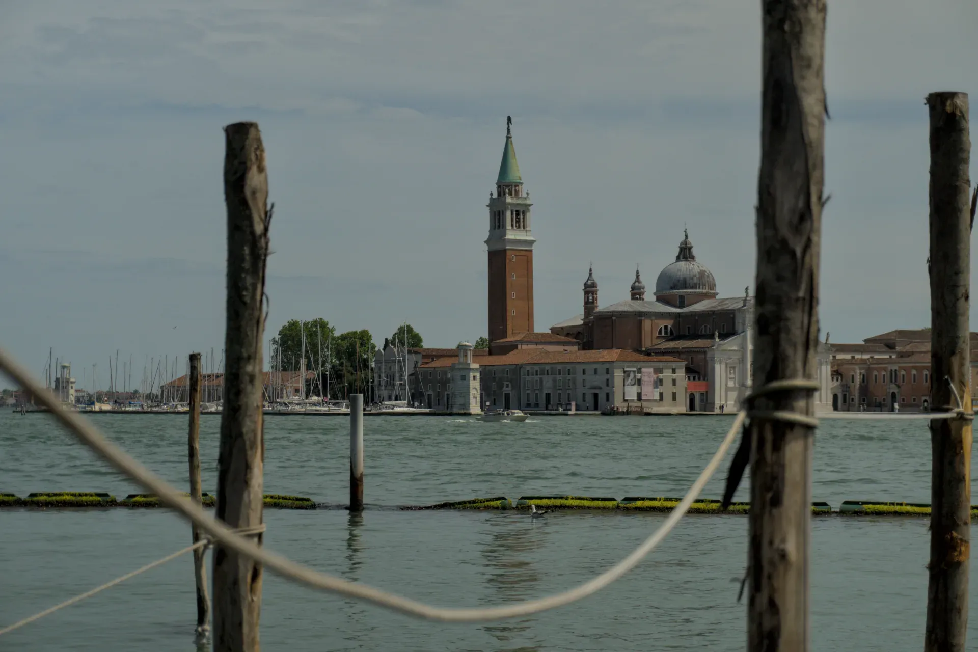 Blick über das Wasser auf die Kirche San Giorgio Maggiore und ihren Glockenturm in Venedig, eingefangen durch Holzpfähle und Seile.