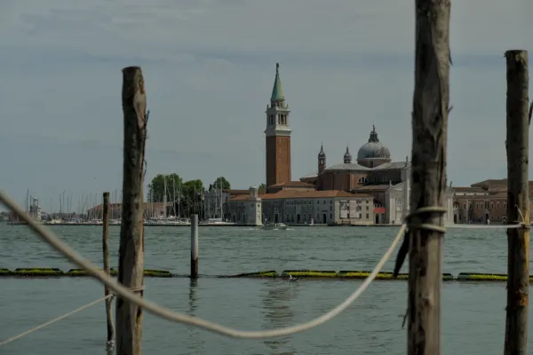 Vue sur l'eau de l'église San Giorgio Maggiore et de son beffroi à Venise, encadrée par des poteaux en bois et des cordes.