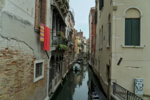 Uno stretto canale veneziano con edifici colorati, panni appesi ai balconi e barche nell'acqua.