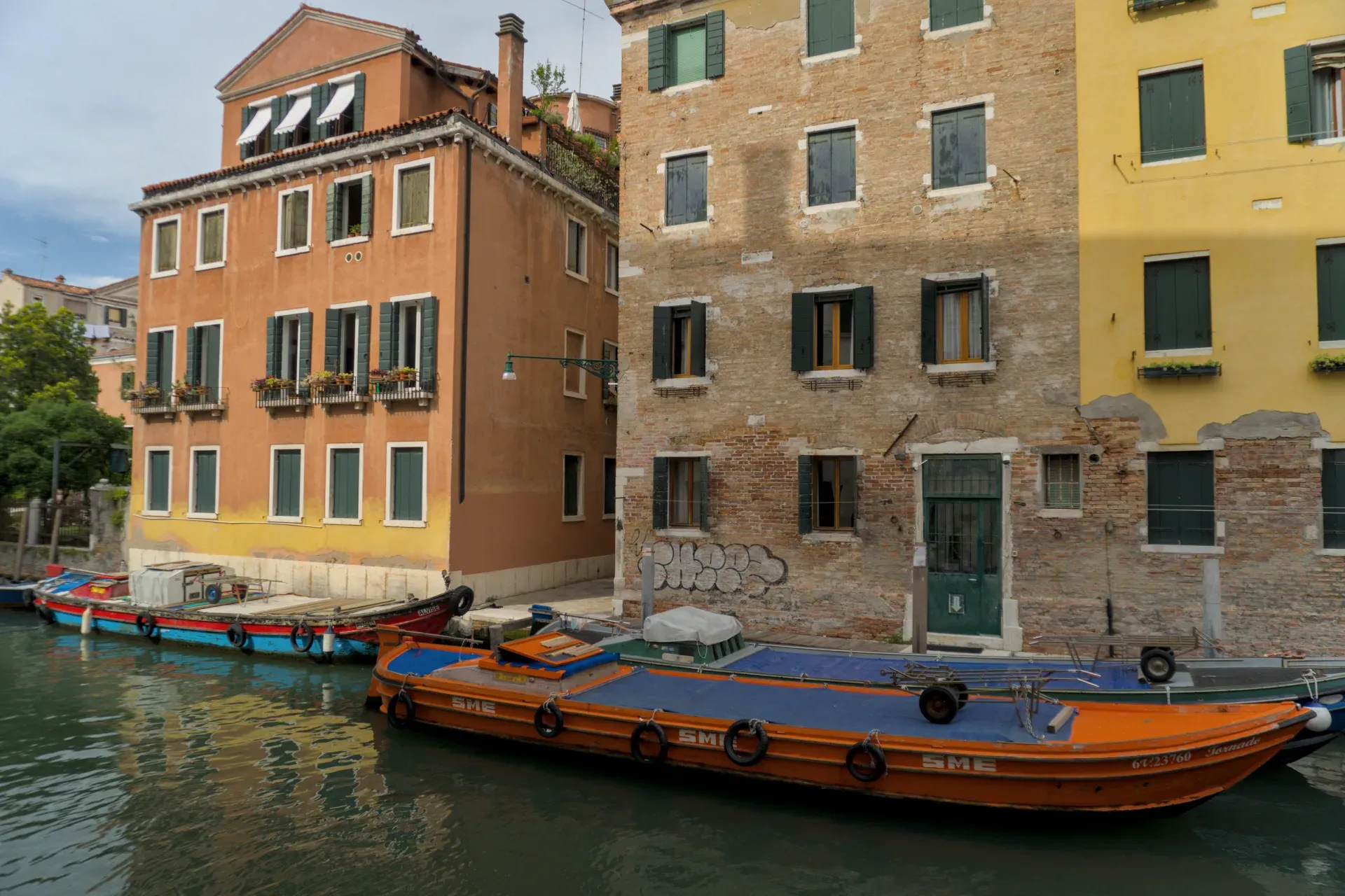 Vista de los canales venecianos con barcos frente a edificios históricos naranjas y amarillos con persianas verdes.