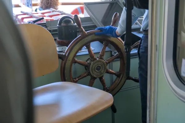 Une roue de gouvernail en bois d'un Vaporetto à Venise, tenue par une personne portant des gants bleus.