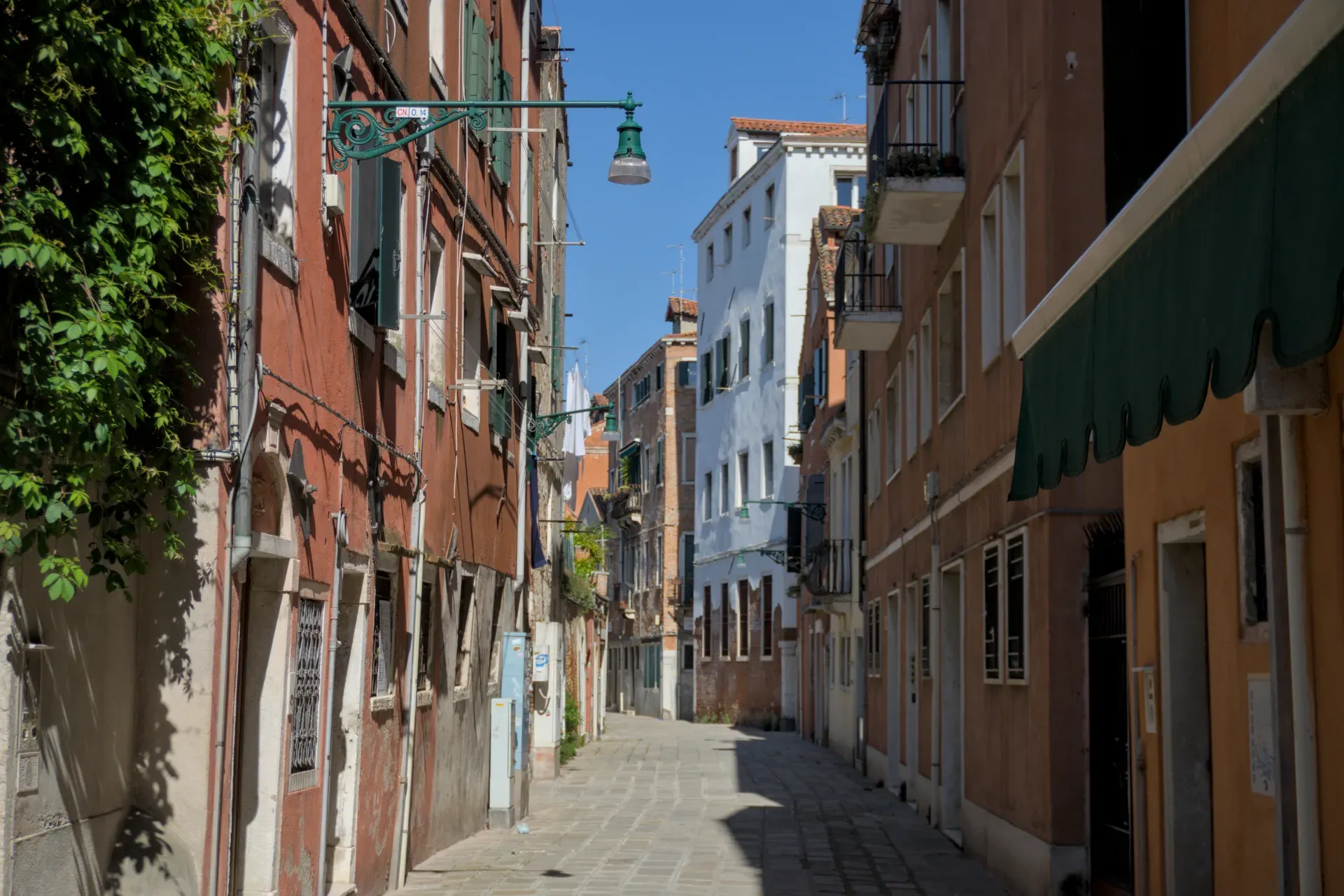 Un vicolo soleggiato e lastricato a Venezia, fiancheggiato da case italiane tradizionali con caldi colori delle facciate.