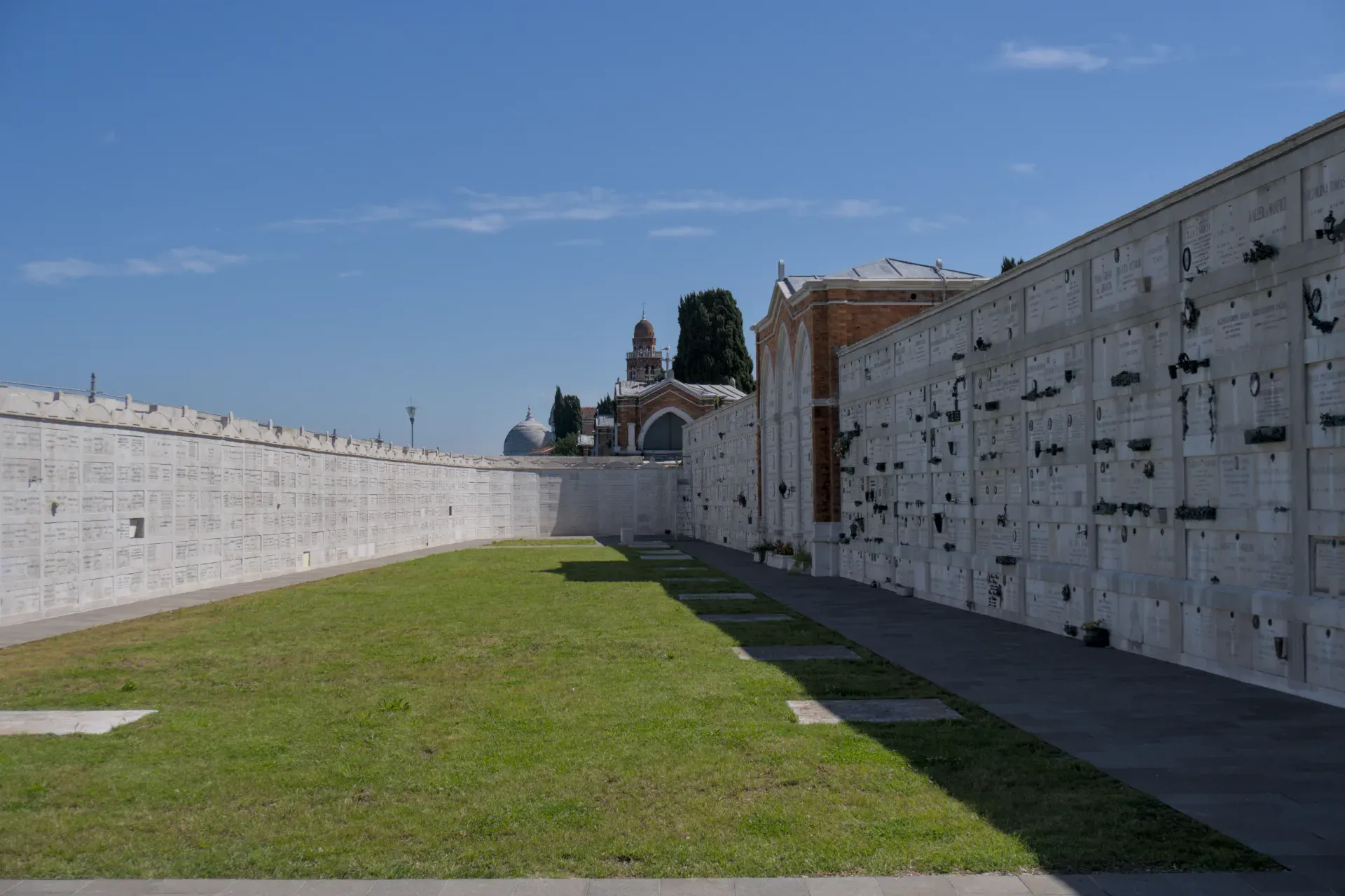 Stampa d'arte delle file di loculi nel cimitero di San Michele, Venezia, con prato verde e sfondo di cielo blu.