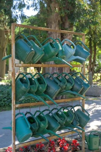 Several green and blue watering cans hang on a rusty rack at San Michele Cemetery.