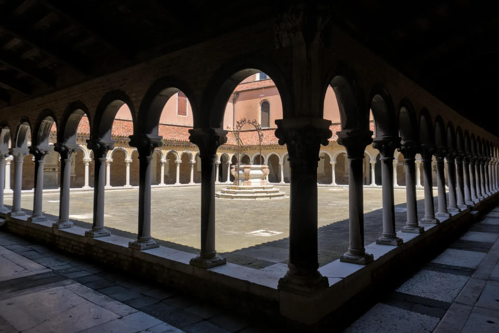 Architektonischer Innenhof auf dem Friedhof San Michele in Venedig mit Bögen, Säulen und einem Brunnen.