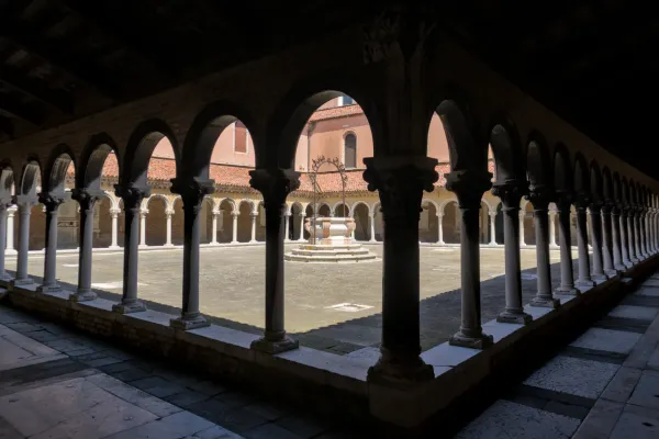 Cour architecturale au cimetière San Michele de Venise avec des arches, des colonnes et un puits.