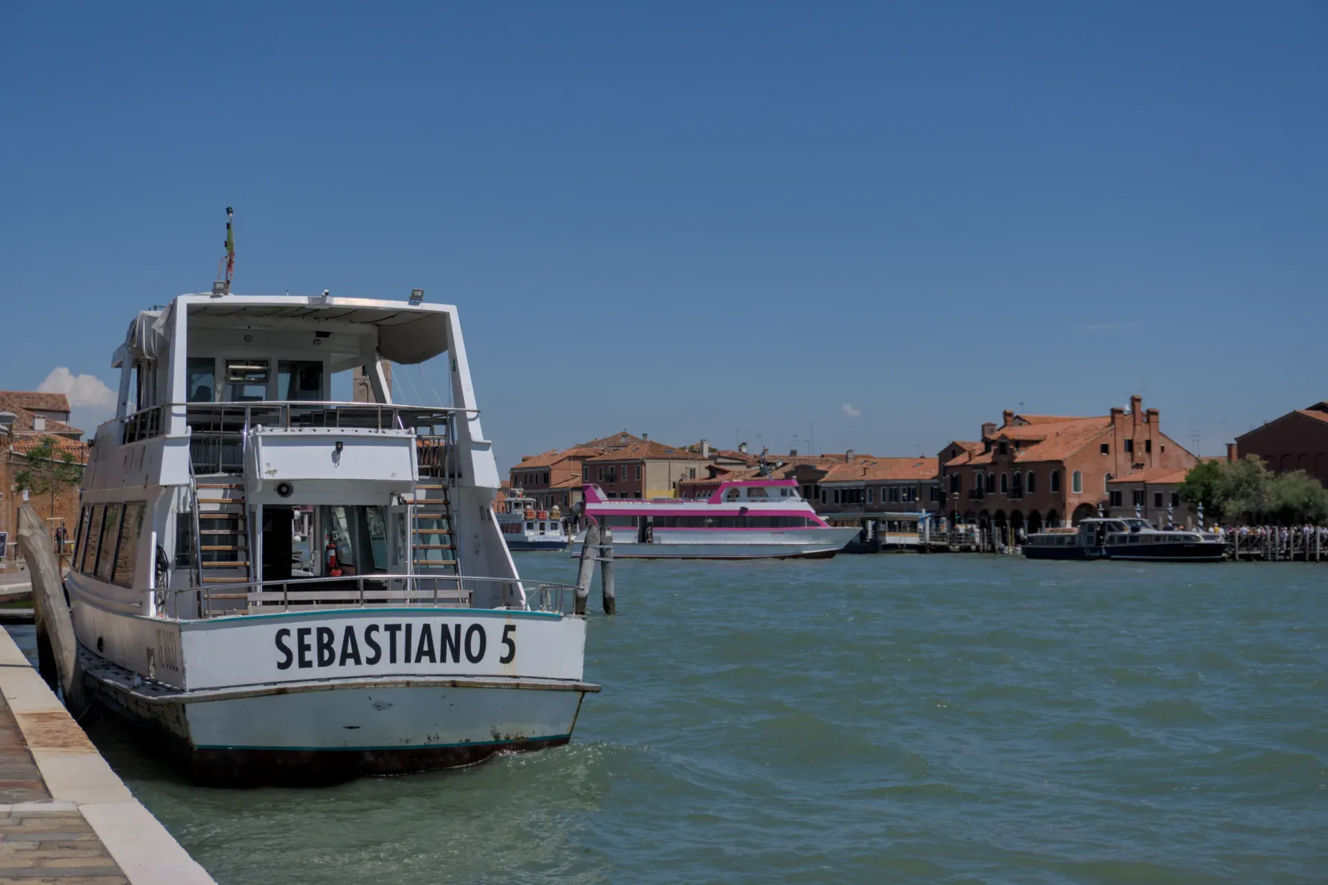 Barche nell'acqua azzurra della laguna di fronte alle case di Murano, Venezia.