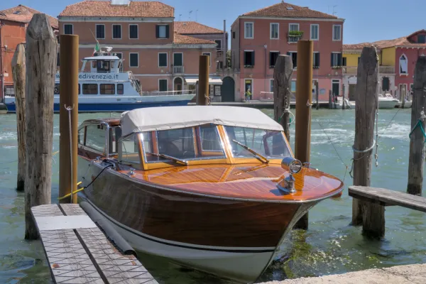 Motoscafo in legno ormeggiato al molo sull'isola di Murano a Venezia, con edifici tradizionali sullo sfondo.