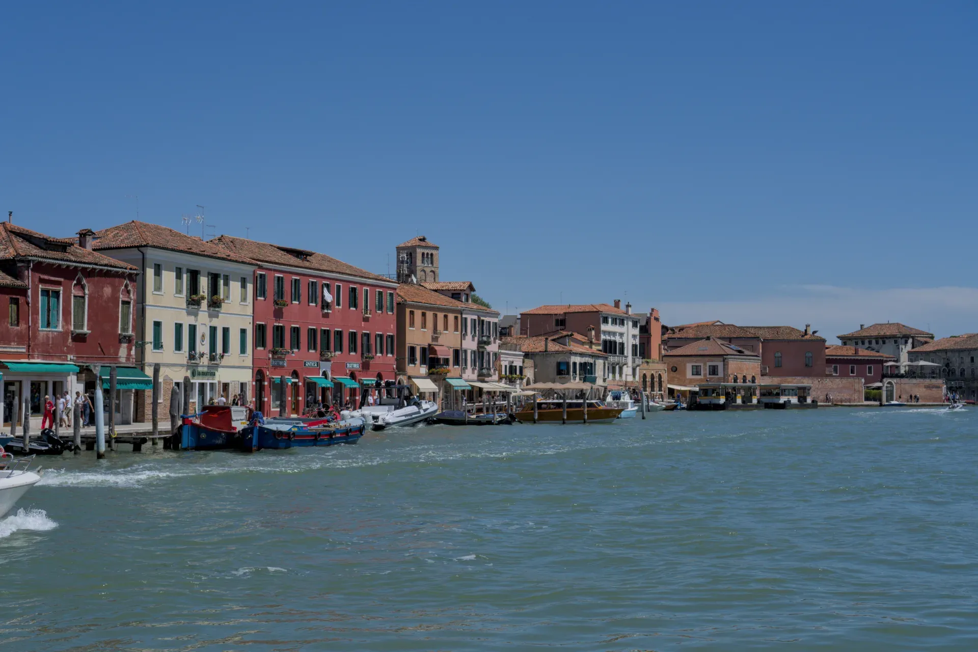 Vue de bâtiments colorés et de canaux sur l'île de Murano, Italie, avec des bateaux dans l'eau et un ciel bleu.