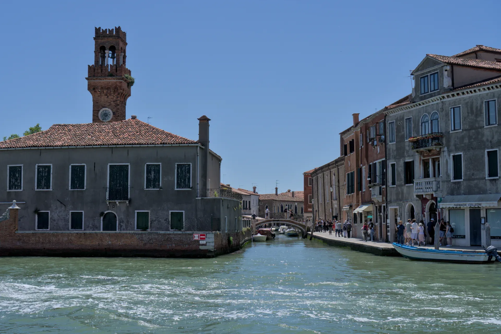 A canal on the island of Murano in Venice with an old brick tower and historic buildings.