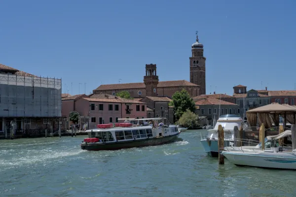 Circulation de bateaux sur le canal de l'île de Murano, Venise, avec des bâtiments d'église historiques en arrière-plan sous le soleil.