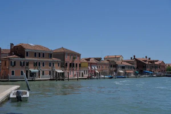 Rangée de bâtiments aux toits de terre cuite au bord de l'eau sur l'île de Murano, Italie, avec une eau bleue calme.