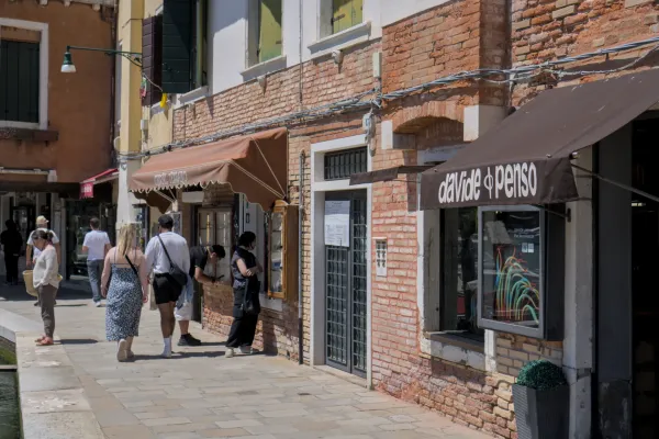 Façade d'une galerie d'art sur l'île de Murano avec des gens qui se promènent devant un jour ensoleillé.