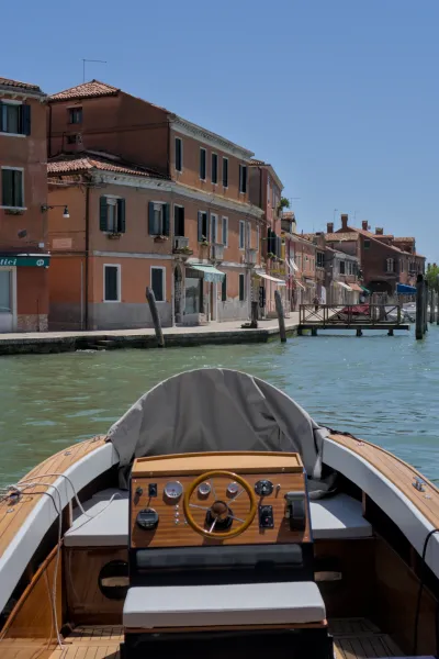 View from the boat onto the canals of Murano, Venice, with traditional buildings and clear sky.