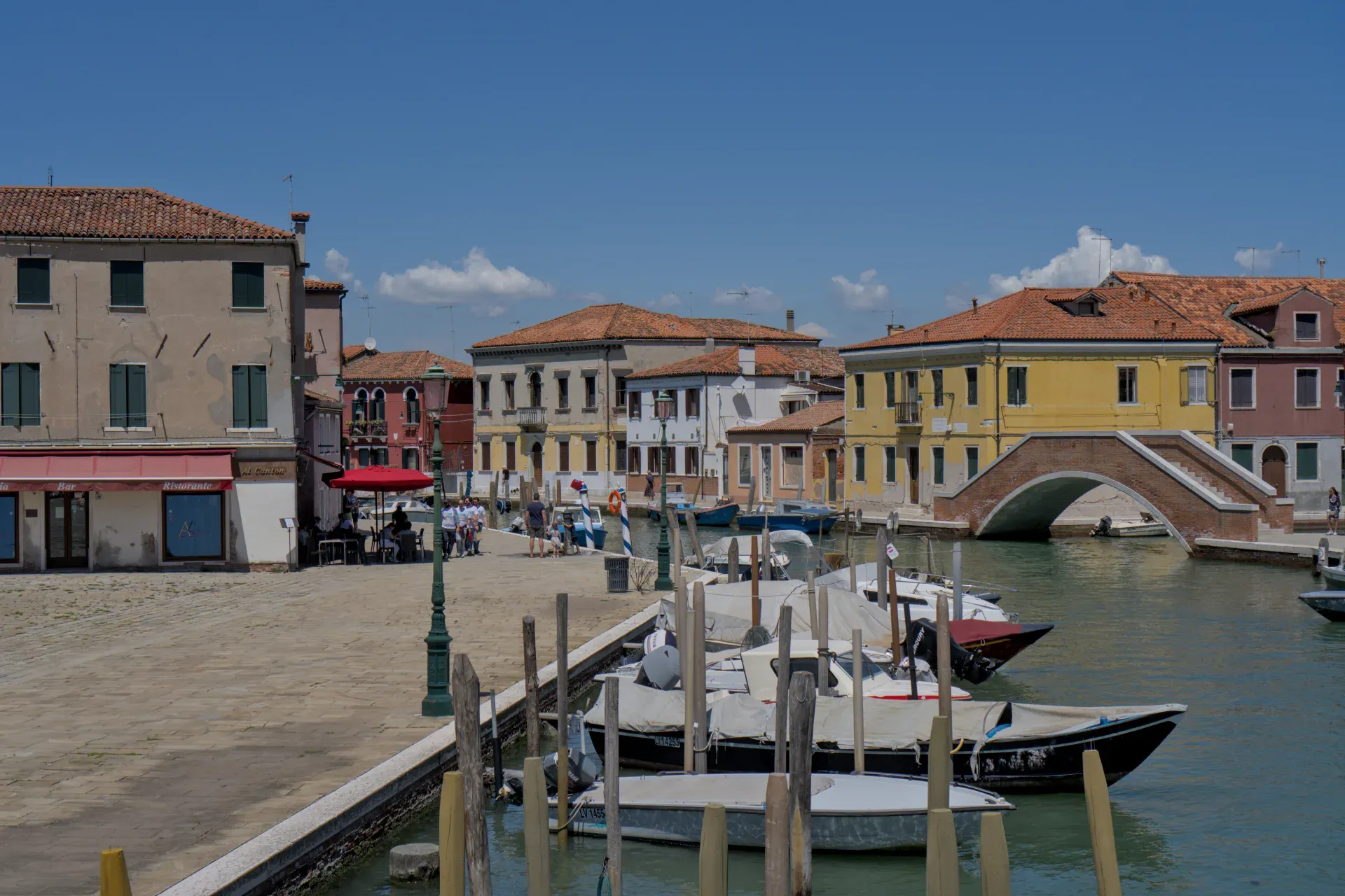 L'île de Murano à Venise présente un canal avec des bateaux et un pont de pierre traditionnel, entouré de maisons colorées.