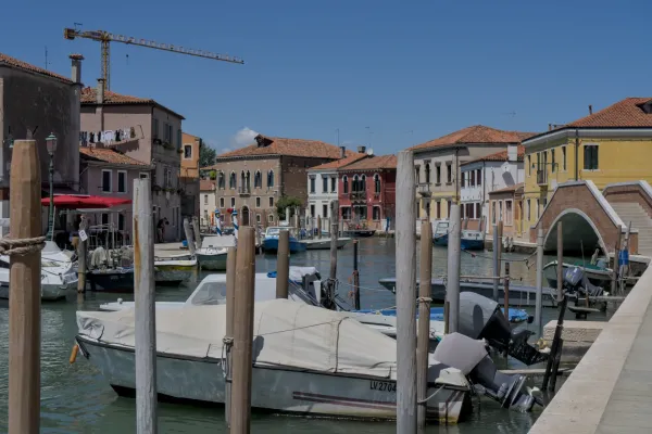 Barche in un canale sull'isola di Murano, Venezia, con case colorate e cielo azzurro.