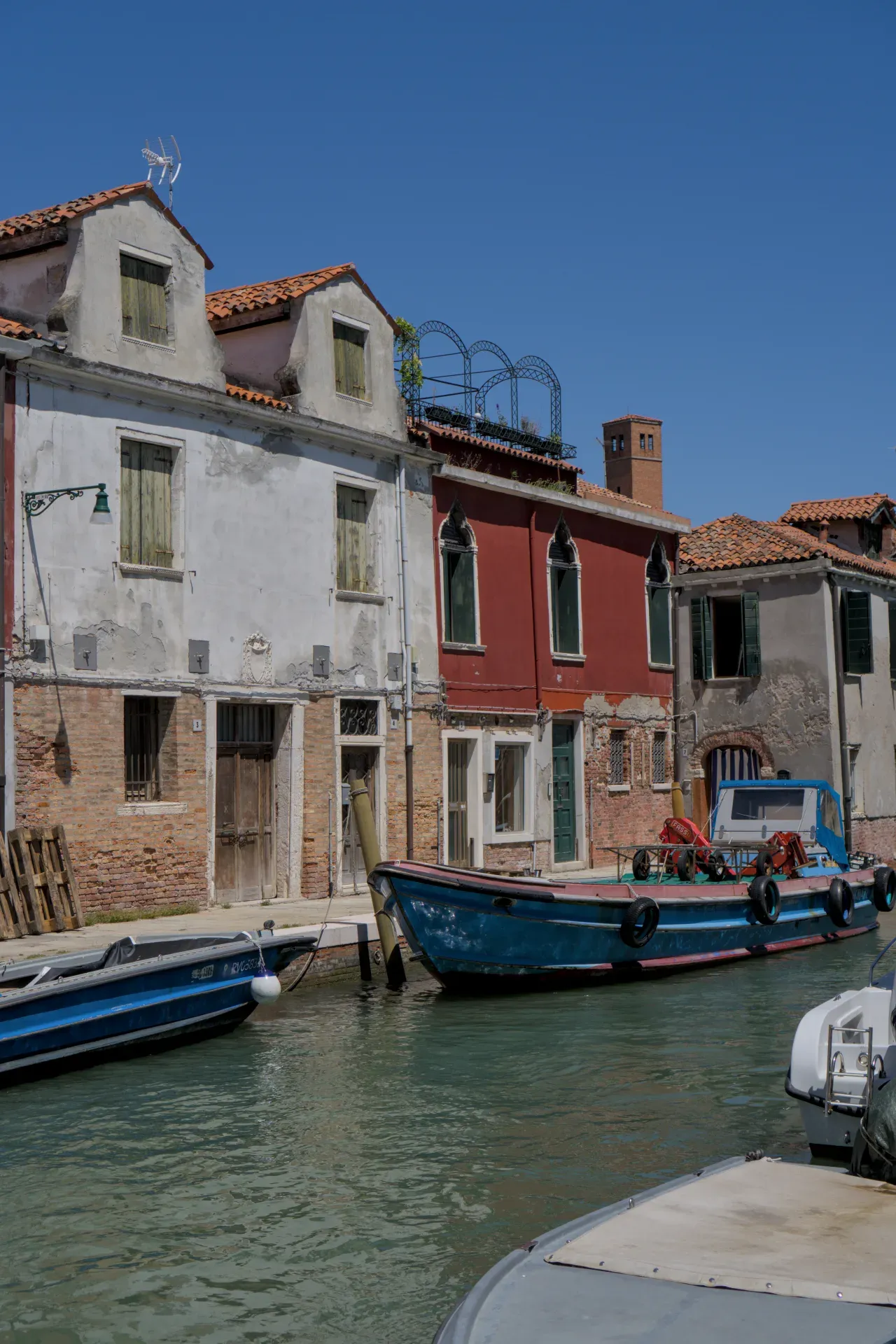 Une ruelle calme sur l'île de Murano à Venise avec des bâtiments traditionnels et des bateaux dans l'eau.