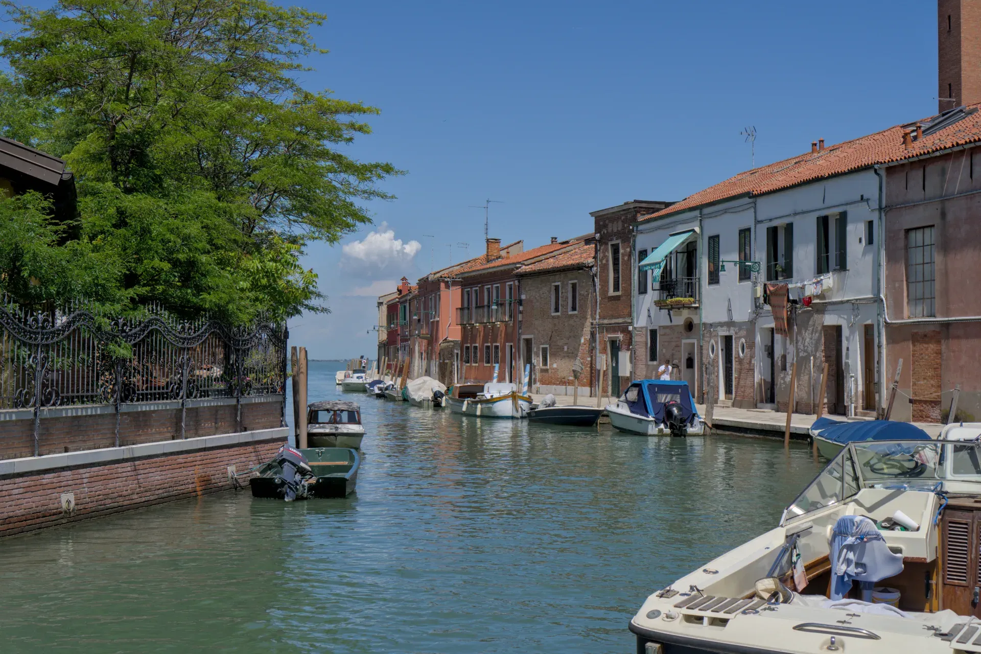 Ein Kanal in Murano, Italien, gesäumt von bunten Häusern und Booten, unter einem strahlend blauen Himmel.