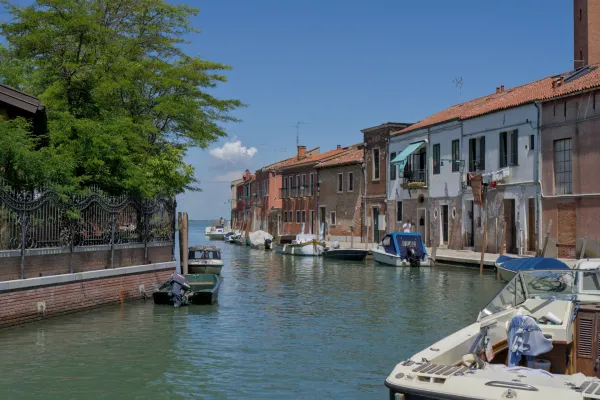 Un canale a Murano, Italia, fiancheggiato da case colorate e barche, sotto un cielo azzurro brillante.