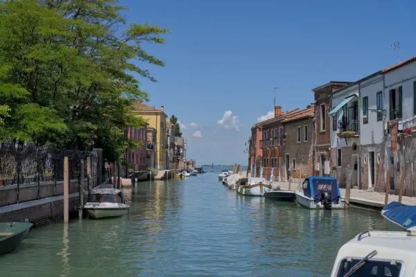 Ein ruhiger Kanal auf der Insel Murano in Venedig, gesäumt von bunten Häusern und Booten im türkisfarbenen Wasser.