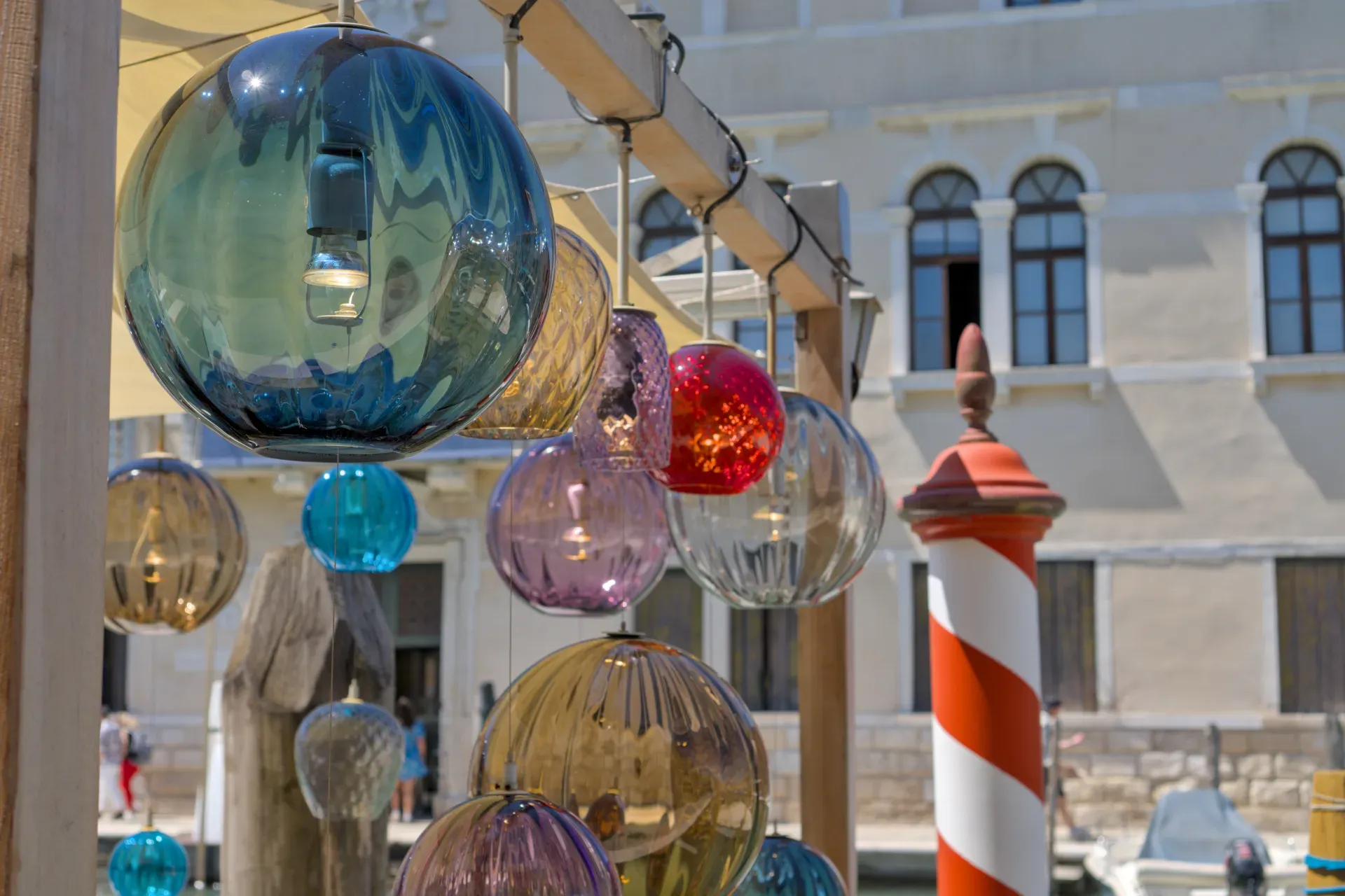 Bunte Murano Glasleuchten, die über einem Kanal in Italien hängen, mit einer Hausfassade im Hintergrund, inspiriert von einem Café.
