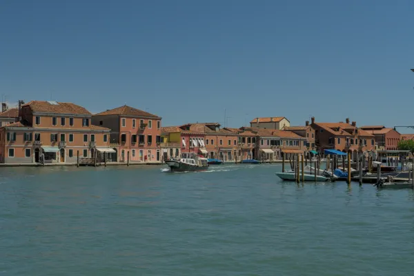 Vista del canale di Murano con case colorate e una barca che passa.