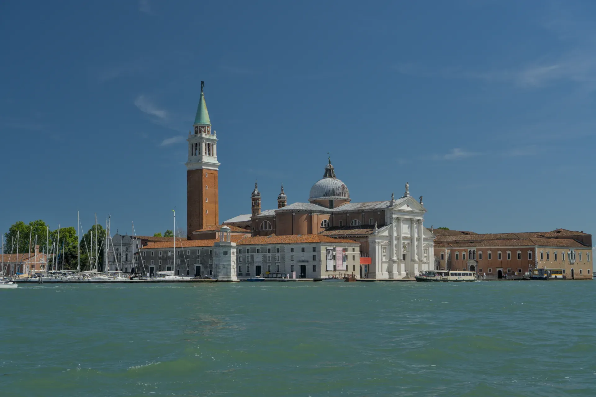 Bazilika San Giorgio Maggiore sa kampanilom u Veneciji, Italija, na pozadini vedrog plavog neba i mirne vode.